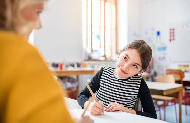 Fleißige Lehrerin lernt mit jungen Schülerinnen im Klassenzimmer, sitzend am Schreibtisch. eine bis eine Stunde. stockfotos