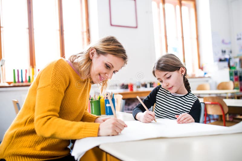 Fleißige Lehrerin lernt mit junger Schülerin im Klassenzimmer, sitzend am Schreibtisch. lizenzfreie stockfotos