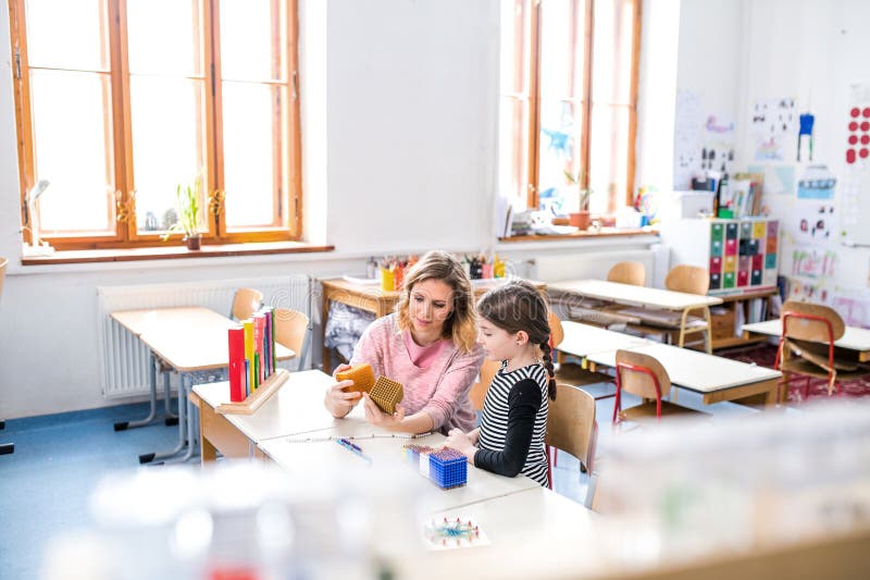 Fleißiger Lehrer, der mit jungen Schülerinnen im Klassenzimmer lernt und Mathematik mithilfe von Lehrmitteln erklärt. stockfotos