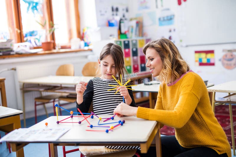 Fleißiger Lehrer, der mit jungen Schülerinnen im Klassenzimmer lernt und Mathematik mithilfe von Lehrmitteln erklärt. stockfoto