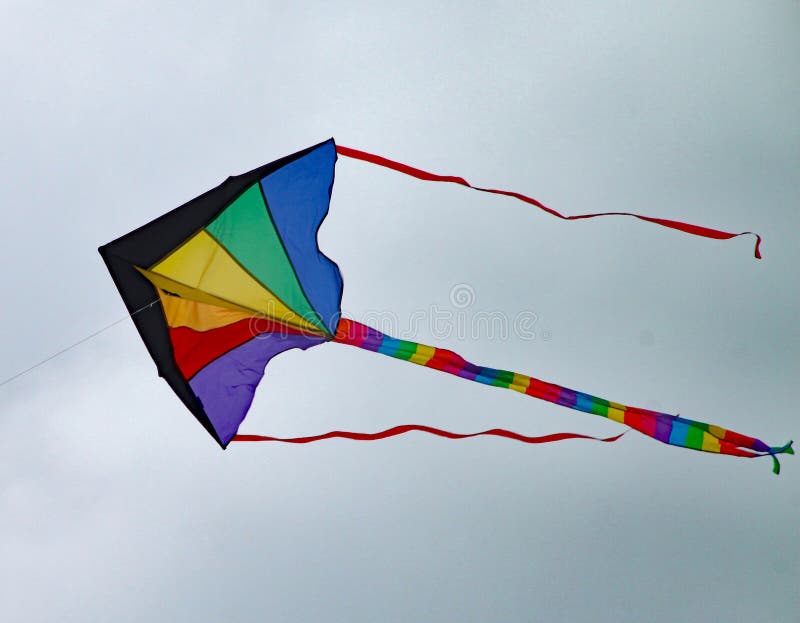 Multi coloured kite with a long tail and two streamers sours high in the sky. Multi coloured kite with a long tail and two streamers sours high in the sky.