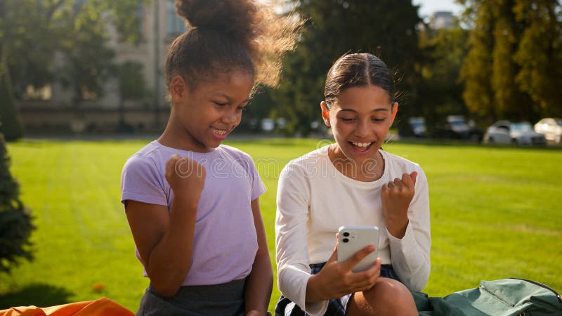 Flerrasiga skolelever skolflickor flickor som använder mobiltelefon utomhus barn afrikanska amerikanska småbarn royaltyfria foton