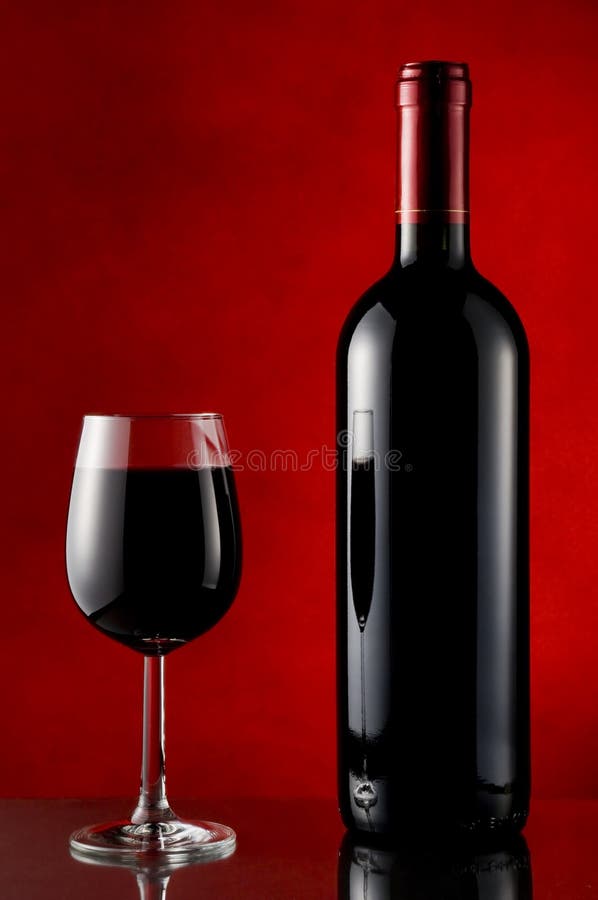 A simple scene with an unopened bottle and filled glass of red wine on a reflective surface against a red background. A simple scene with an unopened bottle and filled glass of red wine on a reflective surface against a red background