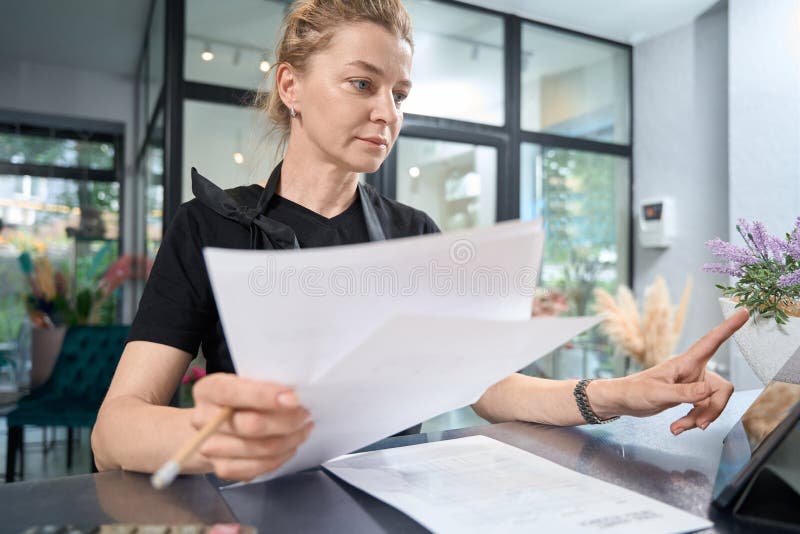 Fleuriste et femme d'affaires réfléchie examiner la paperasse et travailler sur tablette images stock
