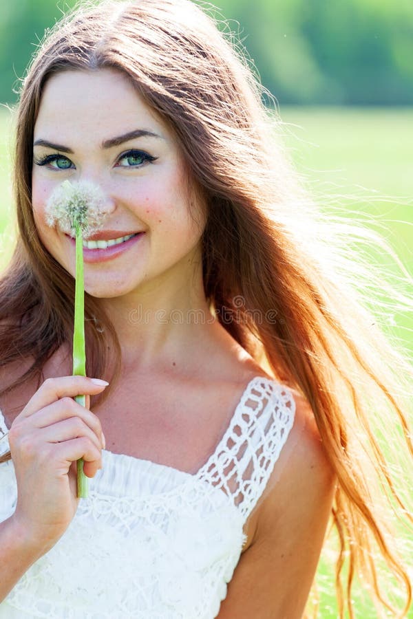 Flicka i vit klänning som håller en dandelion-blomning och ler till dig royaltyfri bild