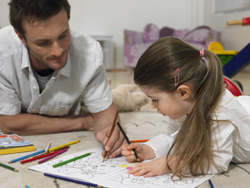 Little girl and father coloring book together on floor at home. Little girl and father coloring book together on floor at home