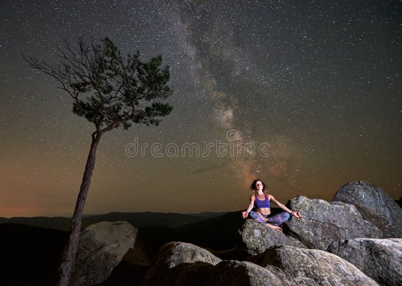 Flicka som bara överst sitter med stängda ögon av den enorma stenblocket som gör yoga arkivbilder Flicka som bara överst sitter med stängda ögon av den enorma stenblocket som gör yoga arkivbilder
