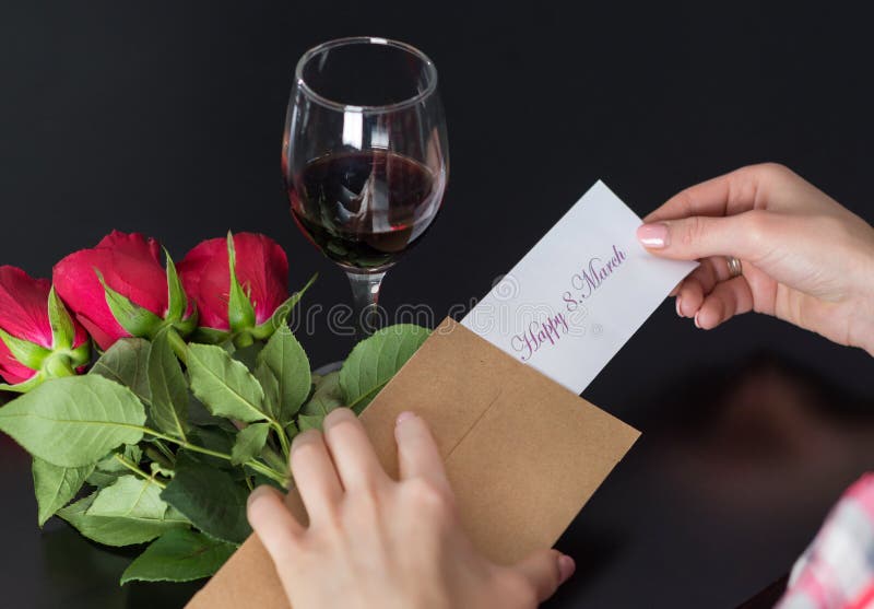 Flickahänder tar ett meddelande lyckliga 8 Mars på papper från det retro kuvertet på det svarta skrivbordet med den röda rosa buk royaltyfri fotografi Flickahänder tar ett meddelande lyckliga 8 Mars på papper från det retro kuvertet på det svarta skrivbordet med den röda rosa buk royaltyfri fotografi
