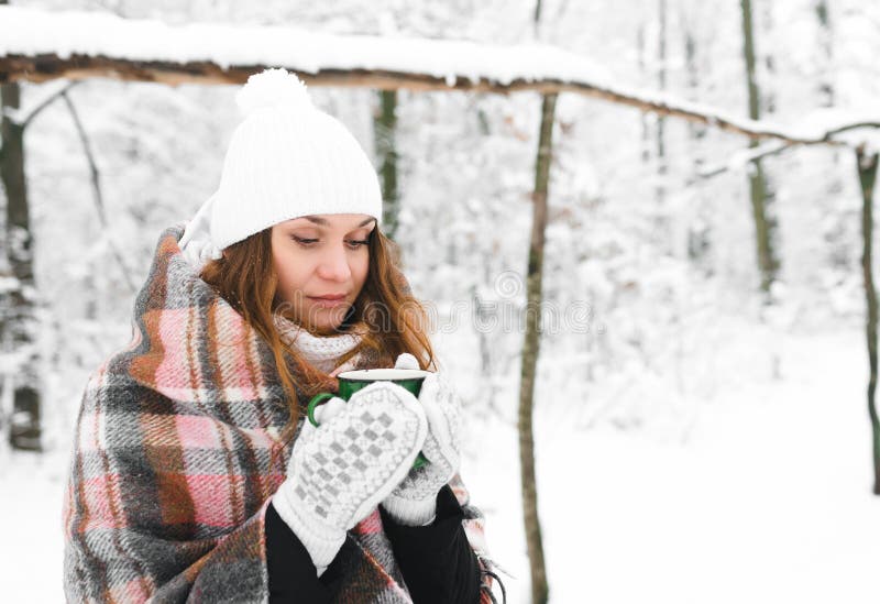 Flickan i en vit hatt som slås in i en filt, rymmer en råna av te i vinter royaltyfria bilder Flickan i en vit hatt som slås in i en filt, rymmer en råna av te i vinter royaltyfria bilder