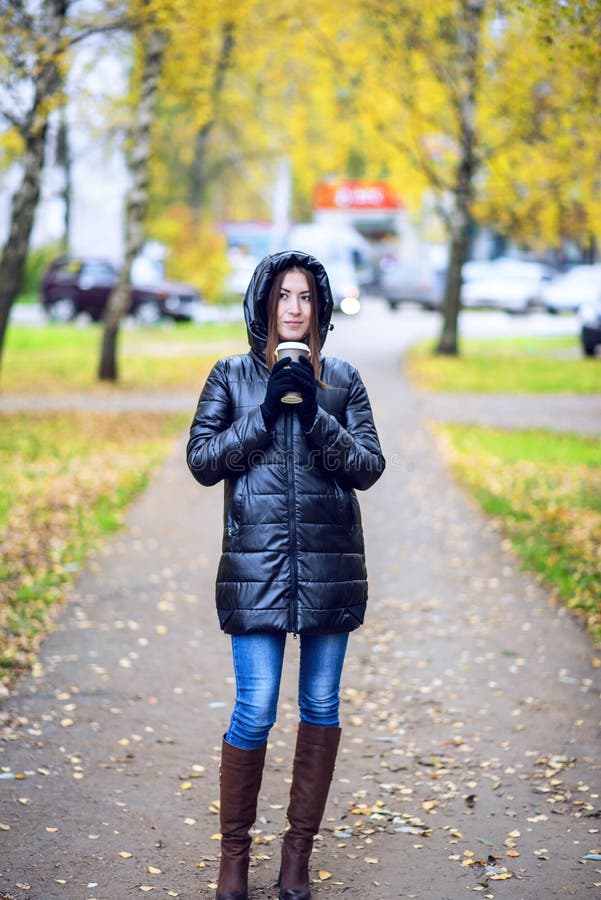 Flickan i omslag med huven och att rymma ett kaffe eller ett te, barn tycker om det fria och sportarna, vårhösten, livsstilen, sv royaltyfri fotografi