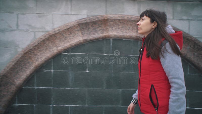 Flickan i sömnlös röd jacka går bredvid murar på grumlig dag