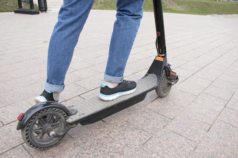 Flickan rider en elektrisk sparkcykel i parkerar vägen, sidosikt r Modernt aktivt royaltyfria bilder Flickan rider en elektrisk sparkcykel i parkerar vägen, sidosikt r Modernt aktivt royaltyfria bilder