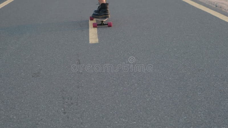 Flickan rider på en skateboard på en ökenväg bland sanddyner. stänga.