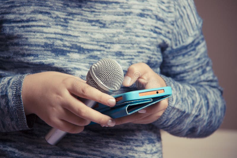 Flickan rymmer en mikrofon i hennes hand och söker efter en sång i telefonen för karaokekapacitet royaltyfria foton Flickan rymmer en mikrofon i hennes hand och söker efter en sång i telefonen för karaokekapacitet royaltyfria foton