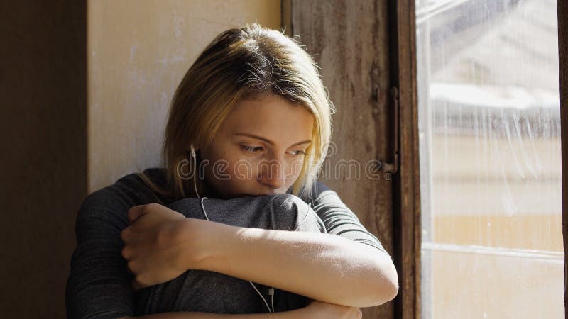 Flickan ser mycket ledsen medan lyssnande musik på hörlurar vid fönstret arkivfoto Flickan ser mycket ledsen medan lyssnande musik på hörlurar vid fönstret arkivfoto