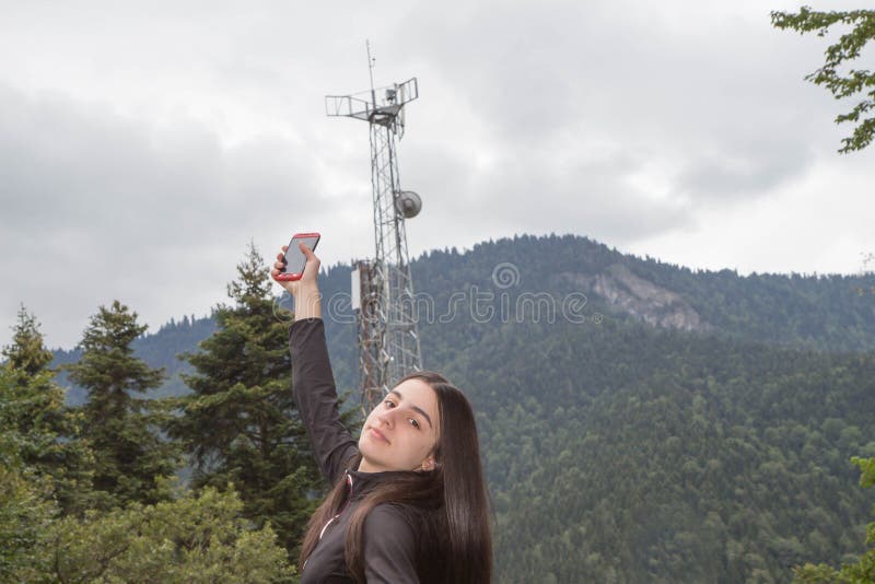 Flickan som använder mobiltelefonen med telekommunikation, står högt med TVantenner och den satellit- maträtten royaltyfri bild Flickan som använder mobiltelefonen med telekommunikation, står högt med TVantenner och den satellit- maträtten royaltyfri bild