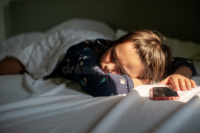Flickan sover med sin telefon i sängen på grund av sitt beroende av den