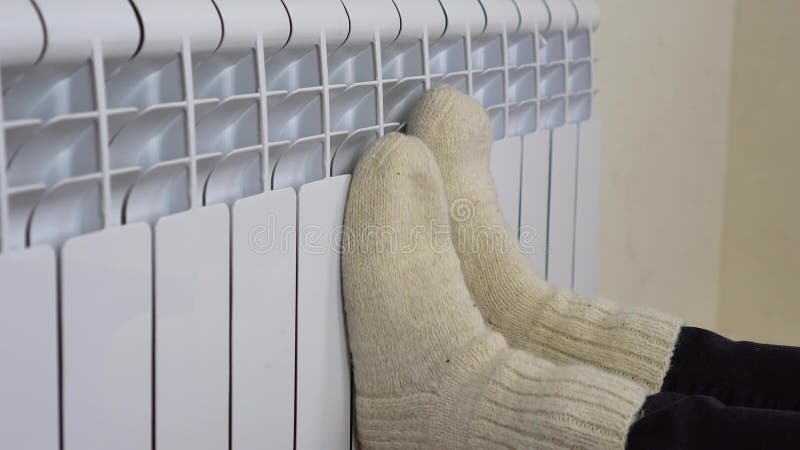 The girl warms her legs on a warm radiator. Close-up of female legs in white woolen socks sent to the radiator. 4k. The girl warms her legs on a warm radiator. Close-up of female legs in white woolen socks sent to the radiator. 4k