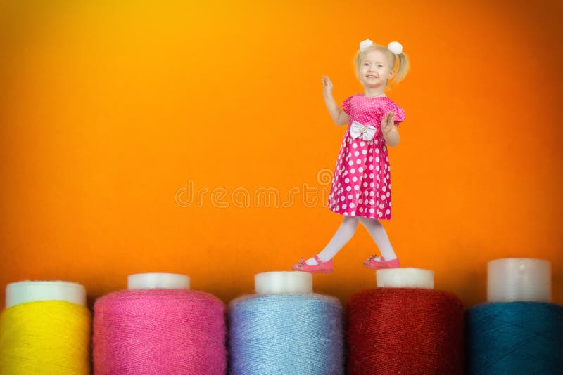 Flickan 3 år balanserar på enorma spolar med trådar arkivfoton
