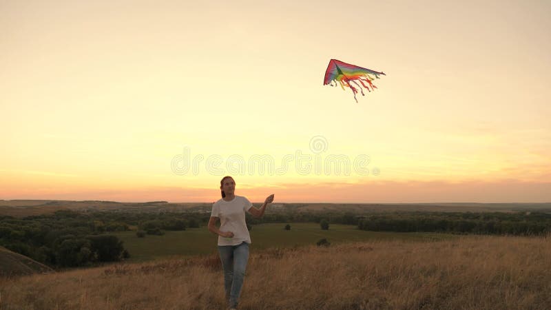 Flickans tonåring skjuter in en flerfärgad drake i himlen Flickan leker med ett leksaksflygplan vid solnedgången i parken hälsosa