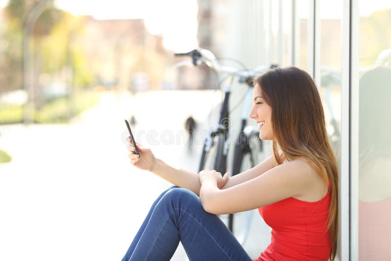 Flickasammanträde genom att använda en mobiltelefon i en parkera royaltyfria foton Flickasammanträde genom att använda en mobiltelefon i en parkera royaltyfria foton