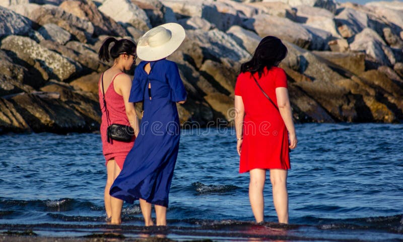 Flickor på stranden i öster som bär en röd och blå klänning med fötterna i vattnet, som tittar på havet slappna av, ett foto tage arkivfoton Flickor på stranden i öster som bär en röd och blå klänning med fötterna i vattnet, som tittar på havet slappna av, ett foto tage arkivfoton
