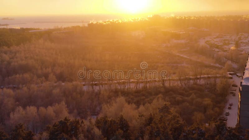 Flight over forest and residential buildings in extreme cold at winter sunset.