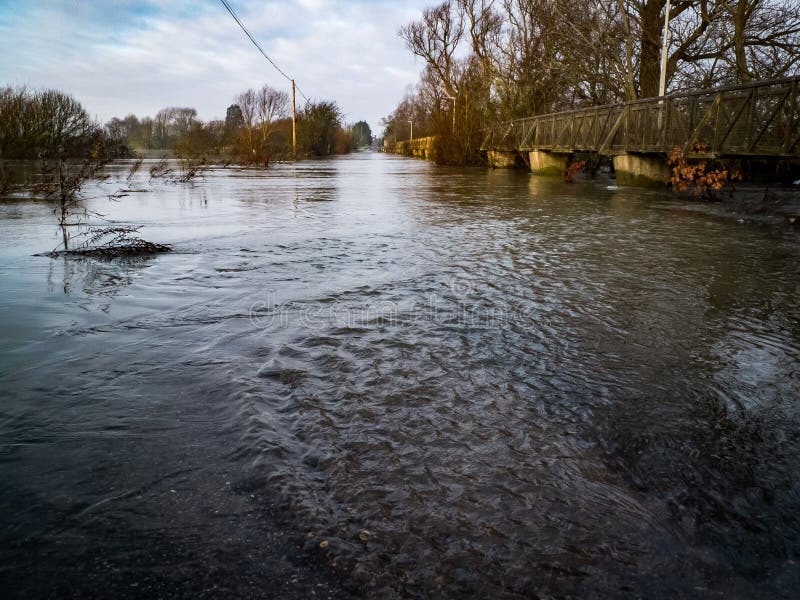 Flooded road with footbridge. Flooded fenland road with access facilitated by adjacent footbridge and trees in Cambridgeshire, United Kingdom stock photography Flooded road with footbridge. Flooded fenland road with access facilitated by adjacent footbridge and trees in Cambridgeshire, United Kingdom stock photography