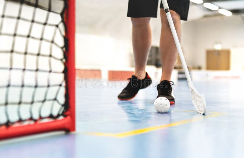 Floorball player. Floor hockey and indoor bandy game. White ball and stick. Goal and net on the floor in training arena.