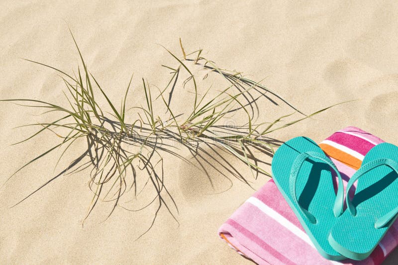 Towel flip-flops/thongs on the sand with beach grass. Towel flip-flops/thongs on the sand with beach grass.