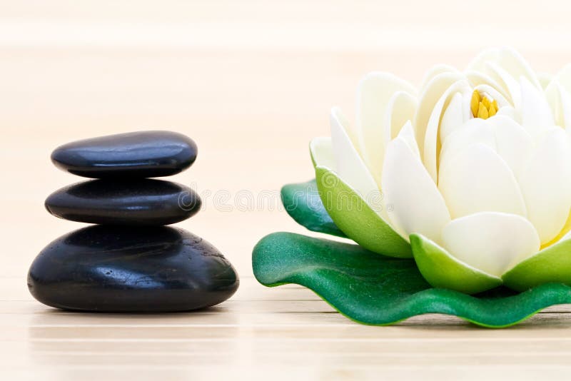 Closeup of black spa stones and an artificial lotus flower on a bamboo mat. Closeup of black spa stones and an artificial lotus flower on a bamboo mat.