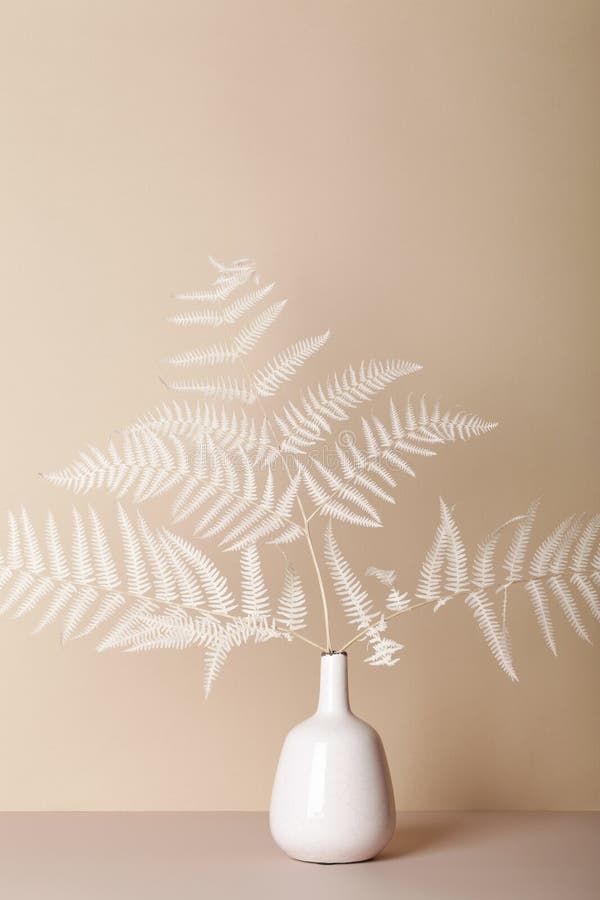 Floral composition of branch fern in vase on beige background