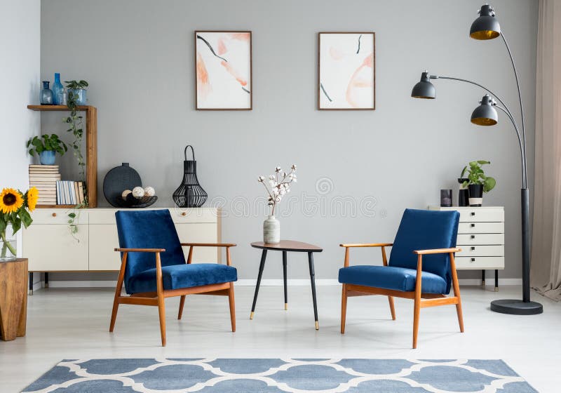 Flores en la tabla de madera entre las butacas azules en interior de la sala de estar con los carteles Foto verdadera fotografía de archivo Flores en la tabla de madera entre las butacas azules en interior de la sala de estar con los carteles Foto verdadera fotografía de archivo