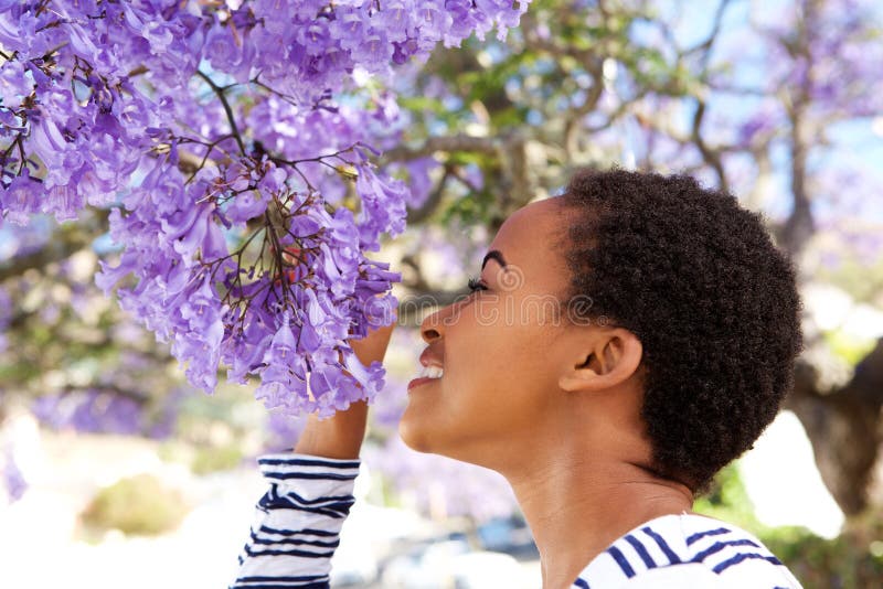 Flores que huelen jovenes de la mujer negra en árbol foto de archivo libre de regalías