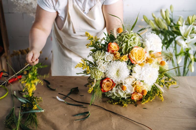 Florist arranges complex bouquet on paper covered table with various botanical stems. Floral education, bouquet building
