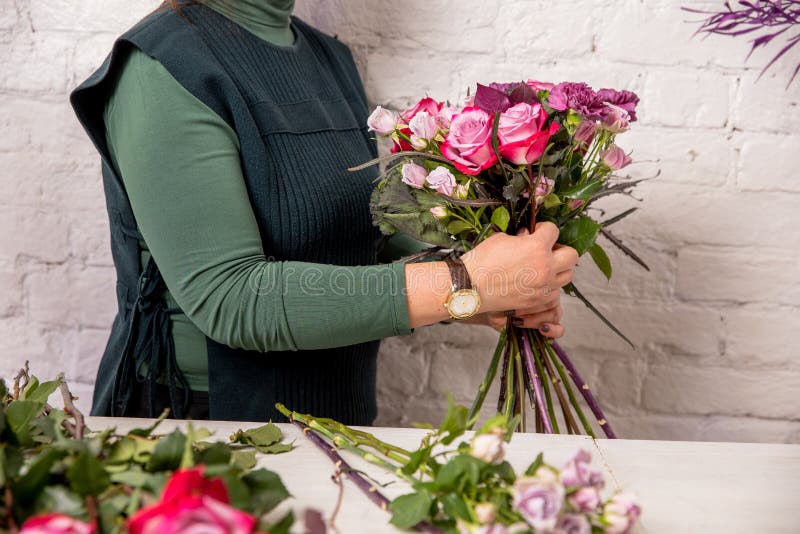 Florist workplace on the background of a white brick wall. The florist makes a bouquet of roses, carnations and eucalyptus, adding