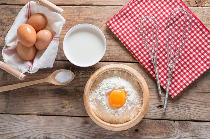 The flour in a wooden bowl, egg, milk and whip for beating.