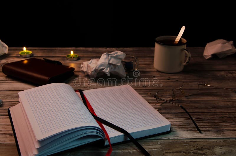 Flour of a writer, search for inspiration. A clean notebook on a wooden table with scattered crumpled paper, a mug of tea, glasses stock images Flour of a writer, search for inspiration. A clean notebook on a wooden table with scattered crumpled paper, a mug of tea, glasses stock images