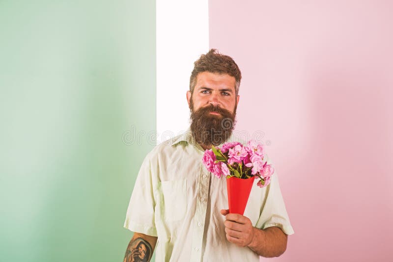Flowers delivery concept. Man with beard calm face holds bouquet fresh flowers. Delivery man with flowers. Hipster with stock photos