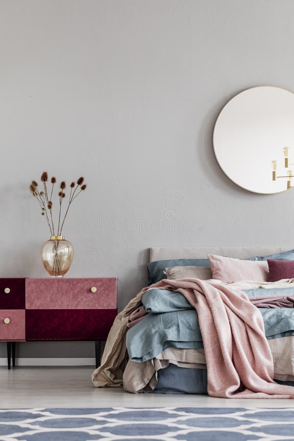 Flowers in elegant glass vase on diy velvet covered pastel pink and burgundy nightstand next to cozy bed with blue and beige royalty free stock image Flowers in elegant glass vase on diy velvet covered pastel pink and burgundy nightstand next to cozy bed with blue and beige royalty free stock image