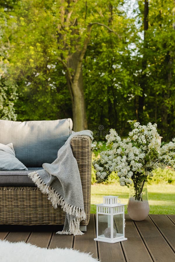 Flowers in vase next to wicker armchair on wooden terrace in green garden