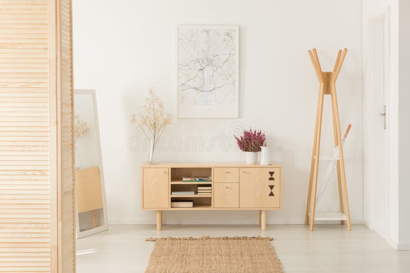 Flowers on wooden cupboard next to rack in white entrance hall interior with poster stock image Flowers on wooden cupboard next to rack in white entrance hall interior with poster stock image
