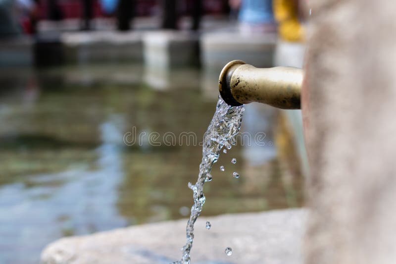 Flusso trasparente di acqua pulita dal rubinetto di rame sullo sfondo alla luce del sole immagini stock