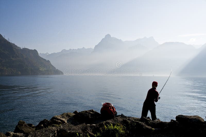 Giovane donna di pesca sulle rive di un lago, in un suggestivo ambiente di acqua e montagne, tra le Alpi Svizzere.