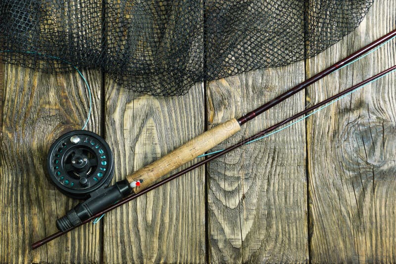 Fly fishing rod ,flie and a landing net on the old wooden table. All ready for fishing.