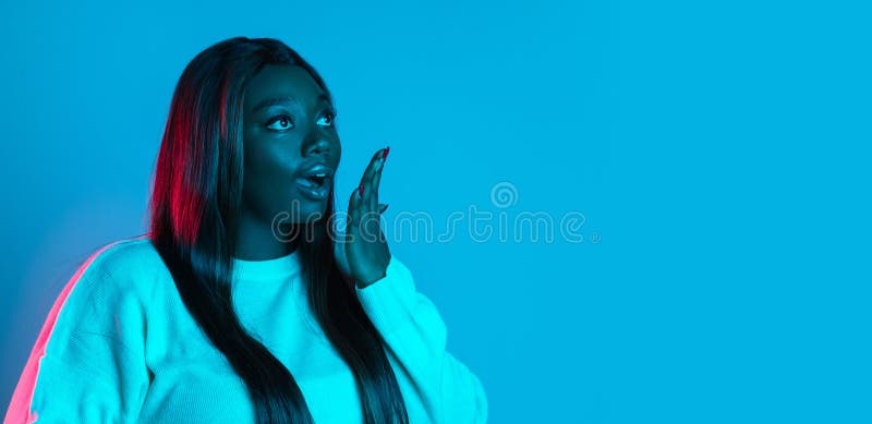 Amazed, delighted. One African beautiful woman with long straight hair isolated on blue studio background in neon light. Concept of human emotions, facial expression. Bodypositive and diversity. Flyer. Amazed, delighted. One African beautiful woman with long straight hair isolated on blue studio background in neon light. Concept of human emotions, facial expression. Bodypositive and diversity. Flyer