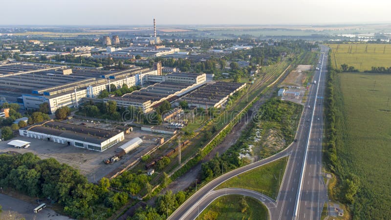 Aerial drone view flight over industrial zone and highway with driving cars on morning. Top view of large logistics park with factories, plants, thermoelectric power station, garages, hangars in city. Aerial drone view flight over industrial zone and highway with driving cars on morning. Top view of large logistics park with factories, plants, thermoelectric power station, garages, hangars in city.