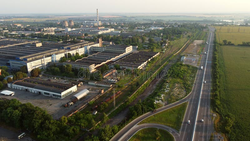 Aerial drone view flight over industrial zone and highway with driving cars on morning. Top view of large logistics park with factories, plants, thermoelectric power station, garages, hangars in city. Aerial drone view flight over industrial zone and highway with driving cars on morning. Top view of large logistics park with factories, plants, thermoelectric power station, garages, hangars in city.