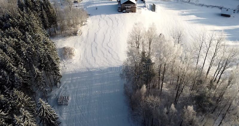 Flying over forest overlooking little wooden house in the meadow. Magical winter