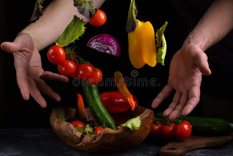 Flying vegetables for salad between male hands. Healthy vegetarian food is levitation over a wooden bowl on a dark stone table royalty free stock photo Flying vegetables for salad between male hands. Healthy vegetarian food is levitation over a wooden bowl on a dark stone table royalty free stock photo